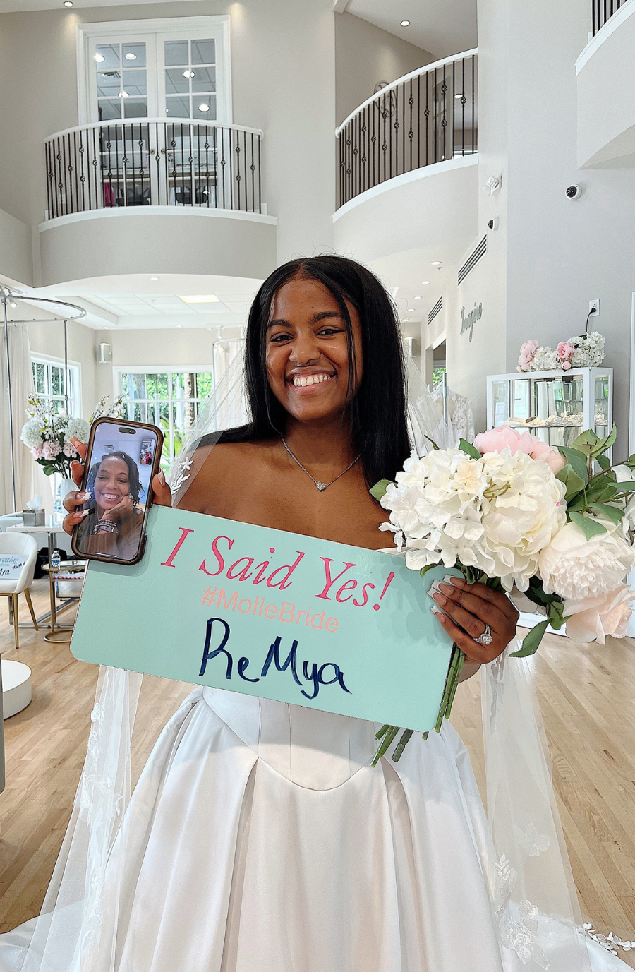 A smiling woman in a wedding dress holding a bouquet of flowers and a sign that says 