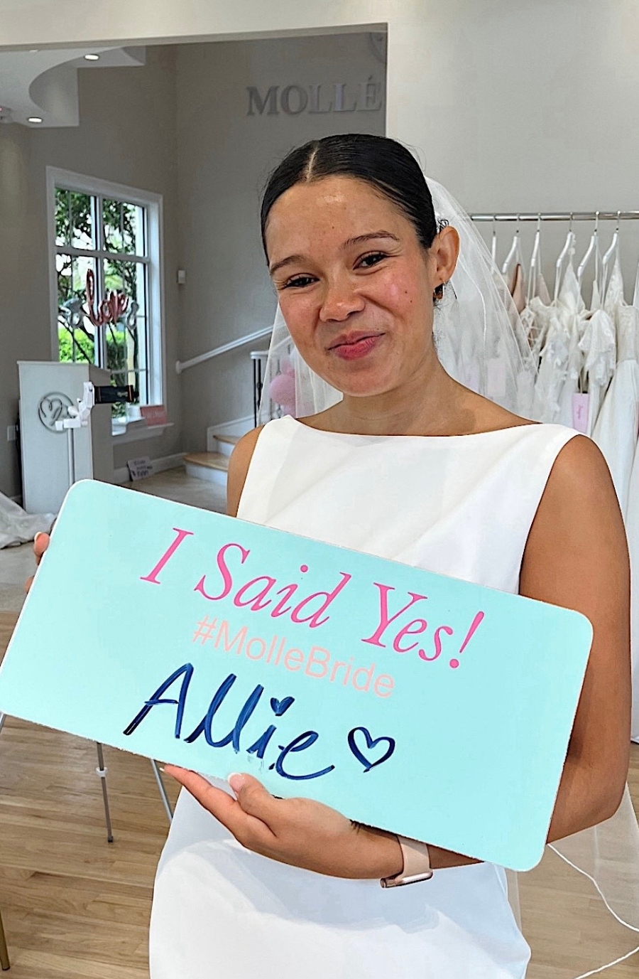 A smiling woman in a white dress holding a sign that says 