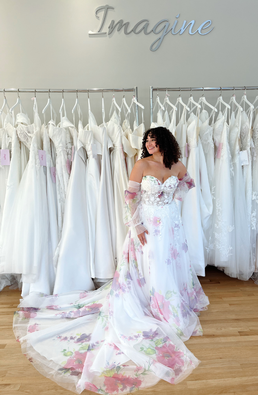Model is wearing an a-line wedding dress with a strapless bodice and off the shoulder detachable sleeves with floral multicolored print