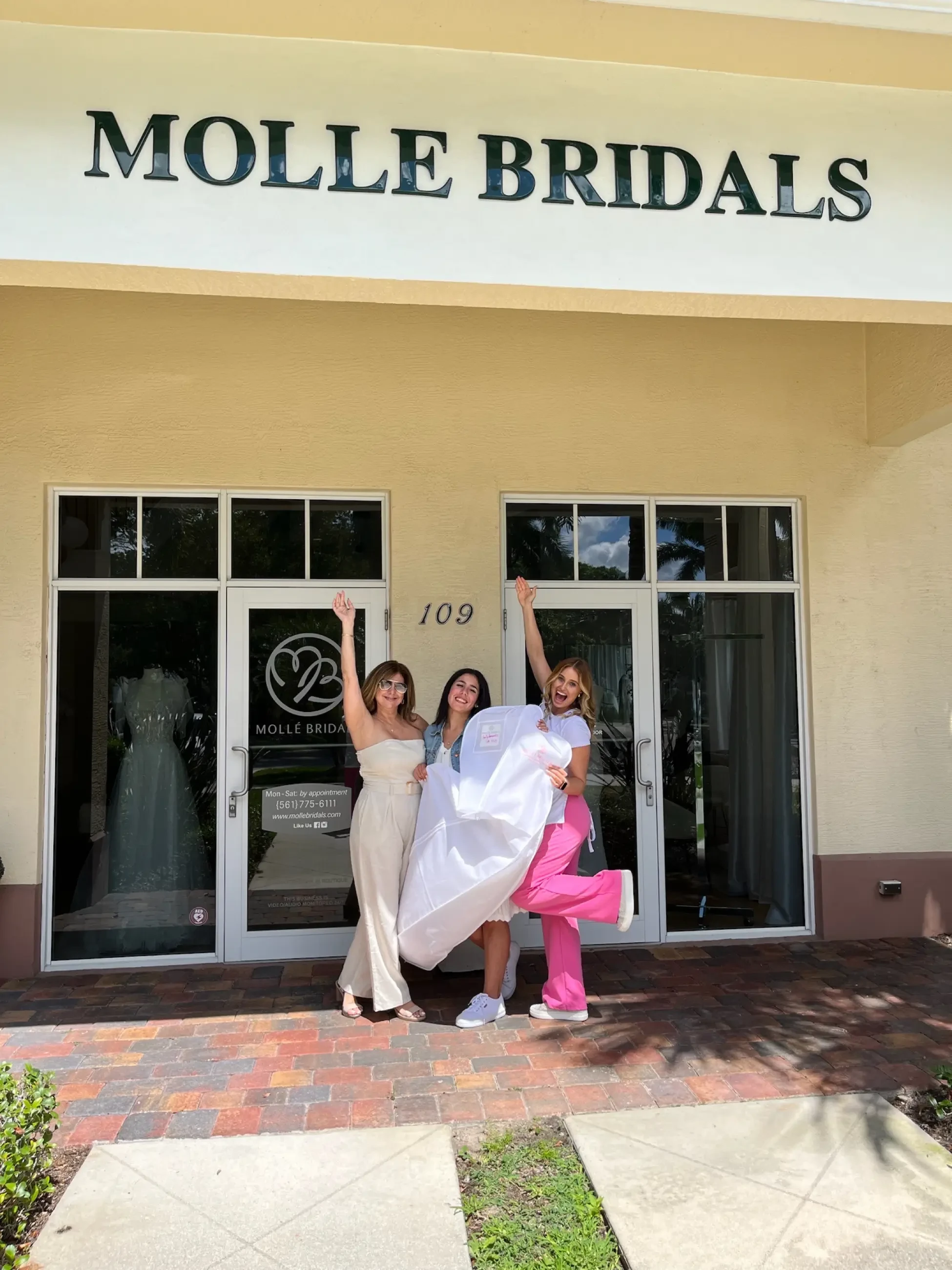 image shows three women excitedly holding a wedding dress garment bag