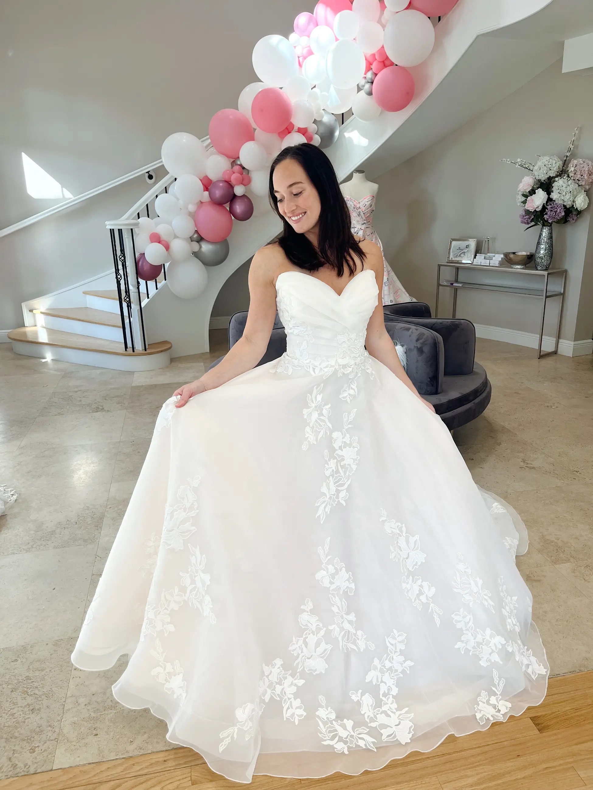 Model is wearing an a-line strapless wedding dress with floral lace on the skirt