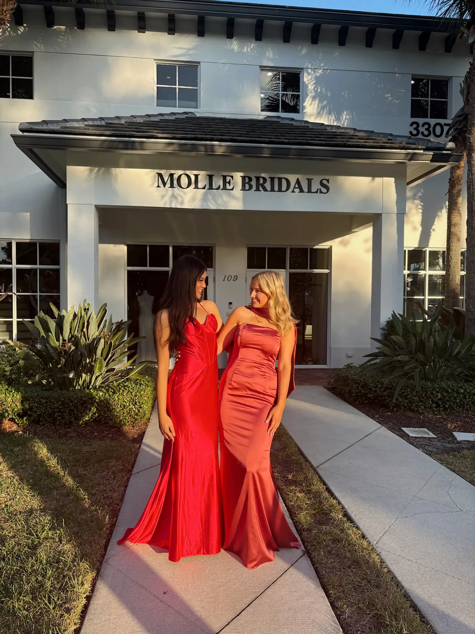 Two women in elegant red dresses stand outside 