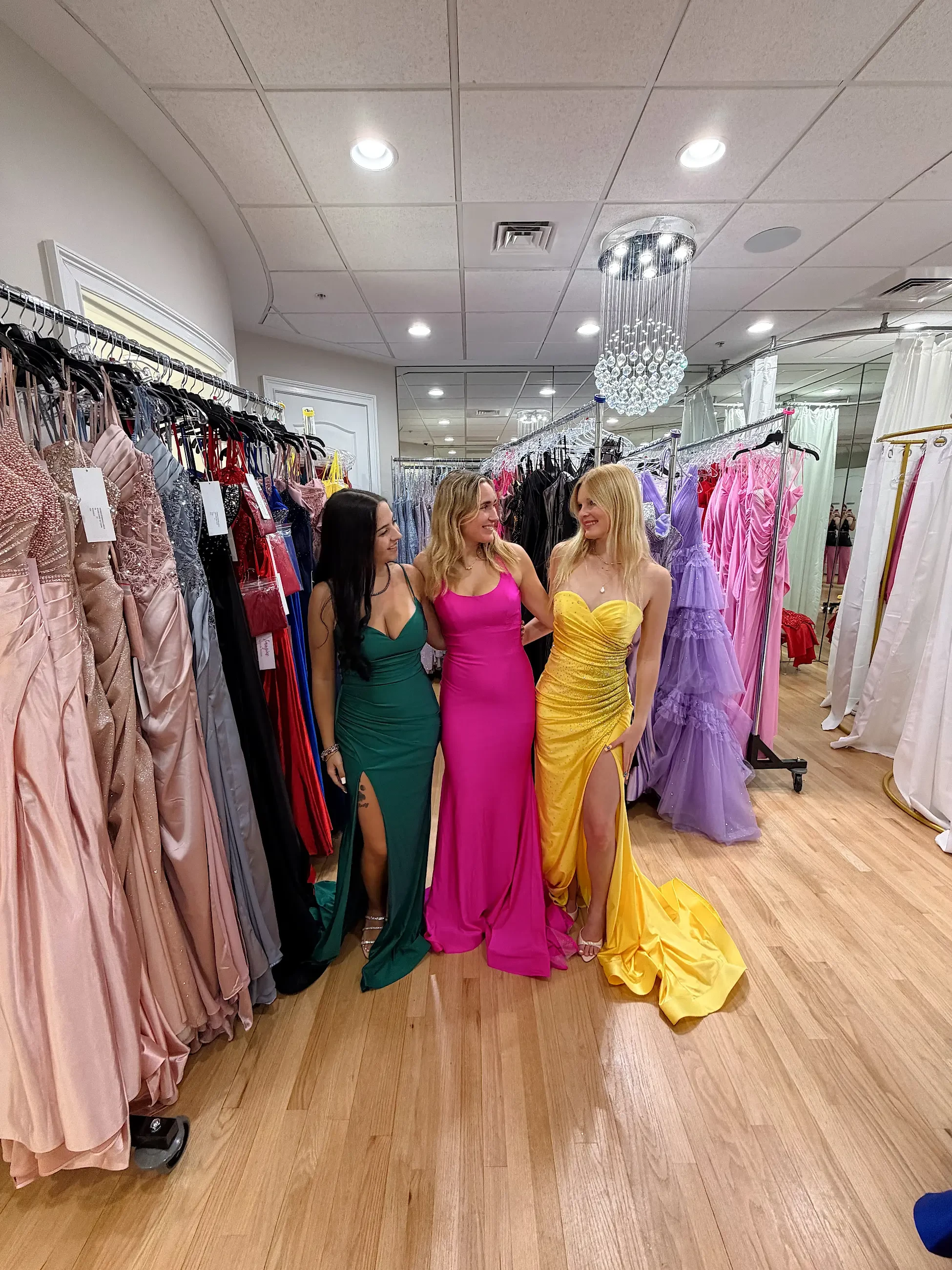 image shows three models wearing colorful prom dresses