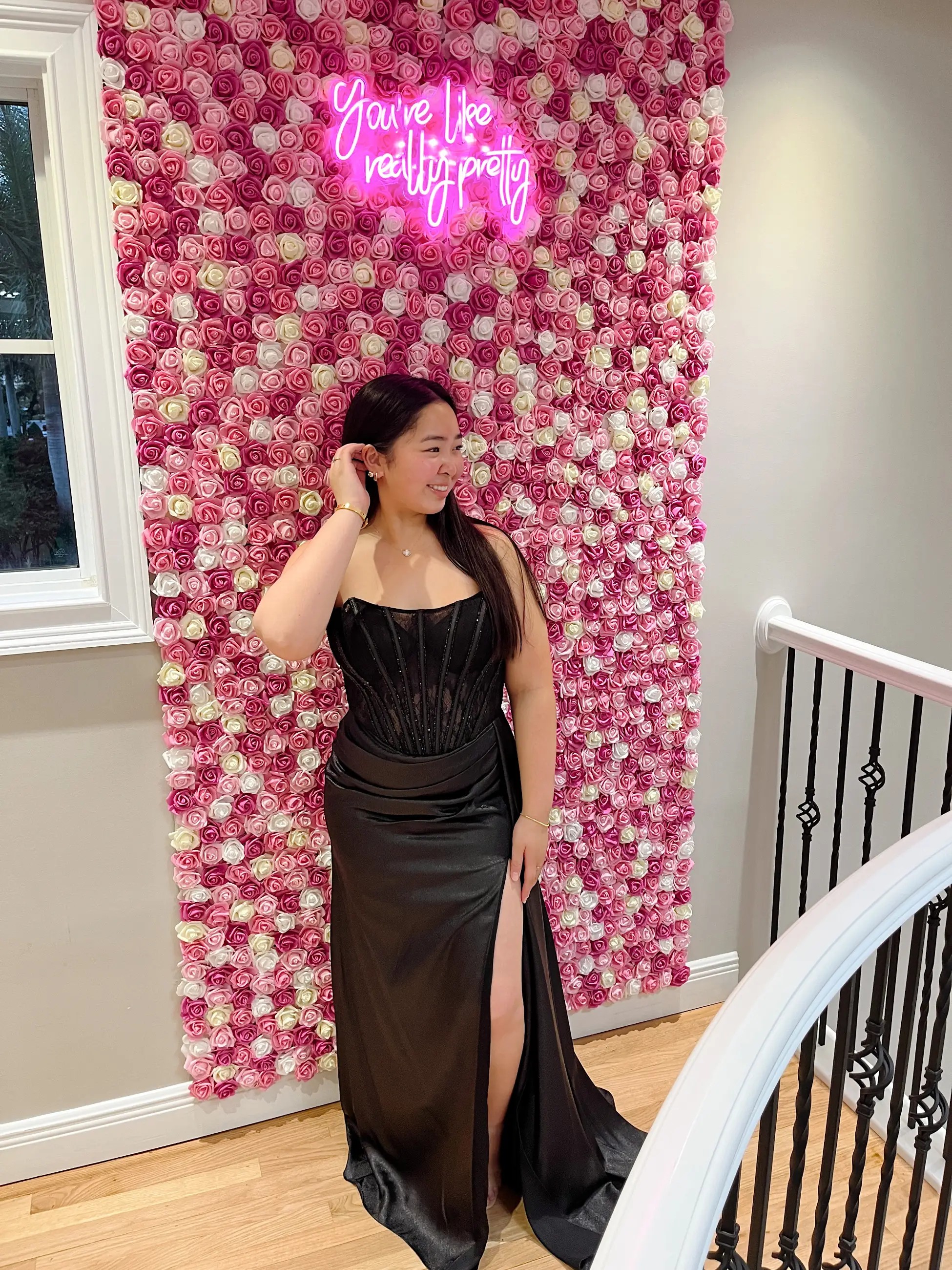 Model is wearing a fitted strapless black evening gown with a corset bodice and thigh high slit