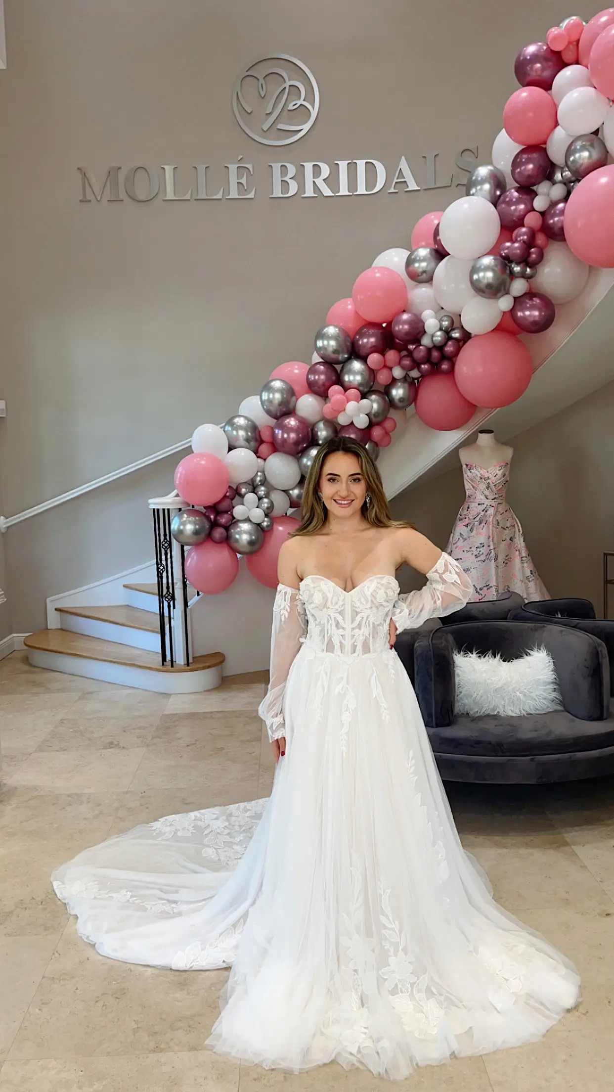 Model is wearing an a-line wedding dress with a strapless bodice and off the shoulder detachable sleeves and a long train