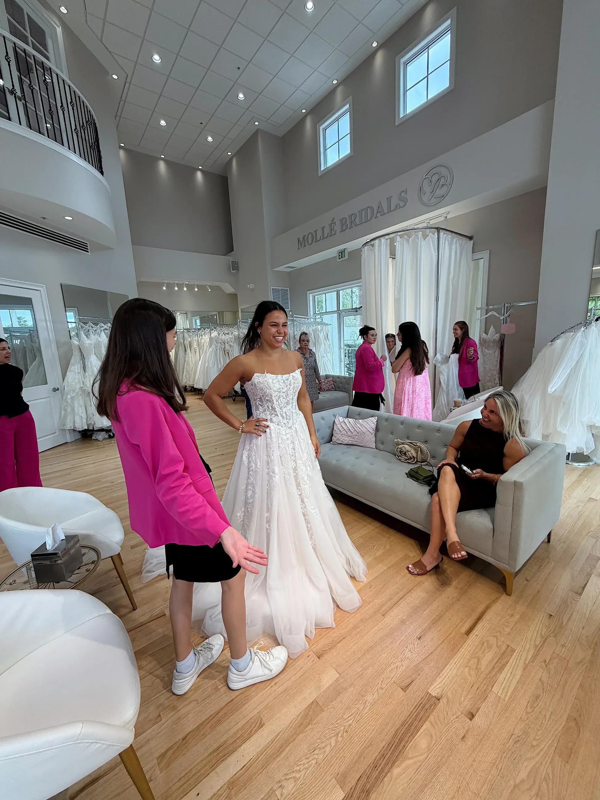 image shows a bridal stylist helping a bride try on wedding gowns
