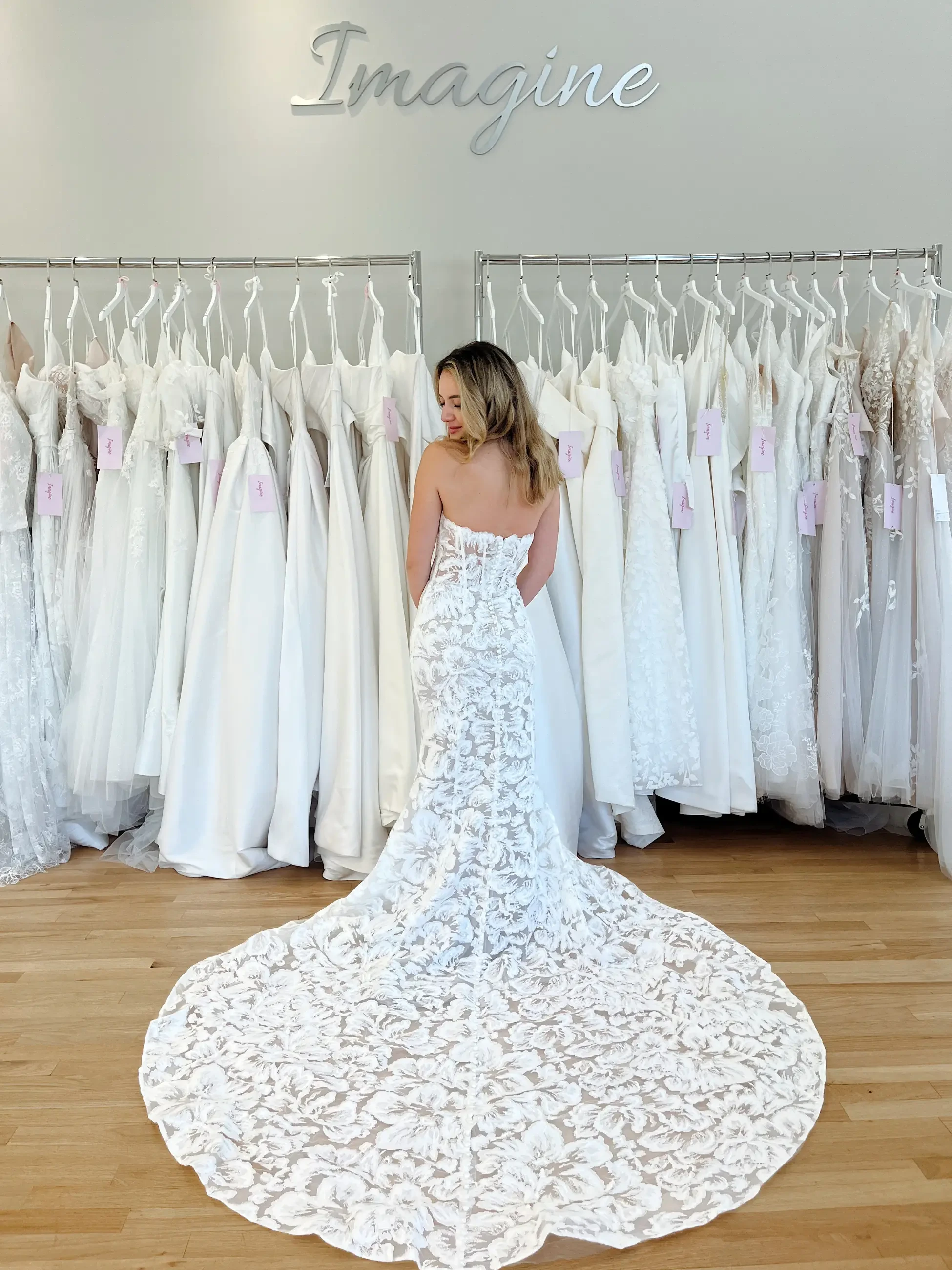 Model is wearing a strapless lace open back wedding dress with a long train