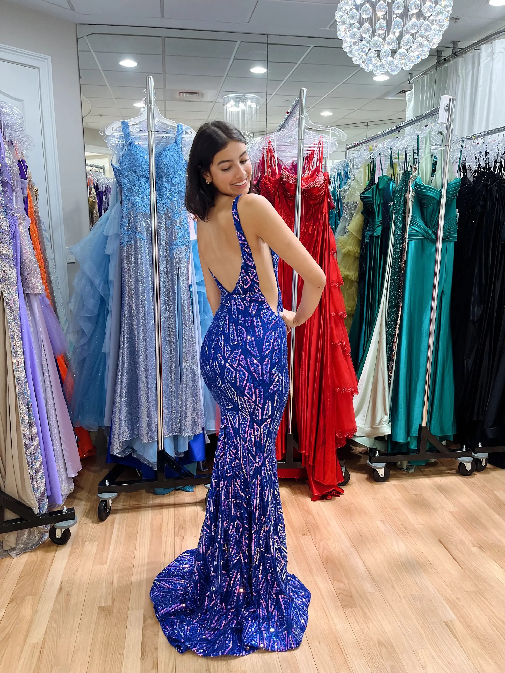 Model is wearing a fitted shimmery dark blue evening gown with an open back