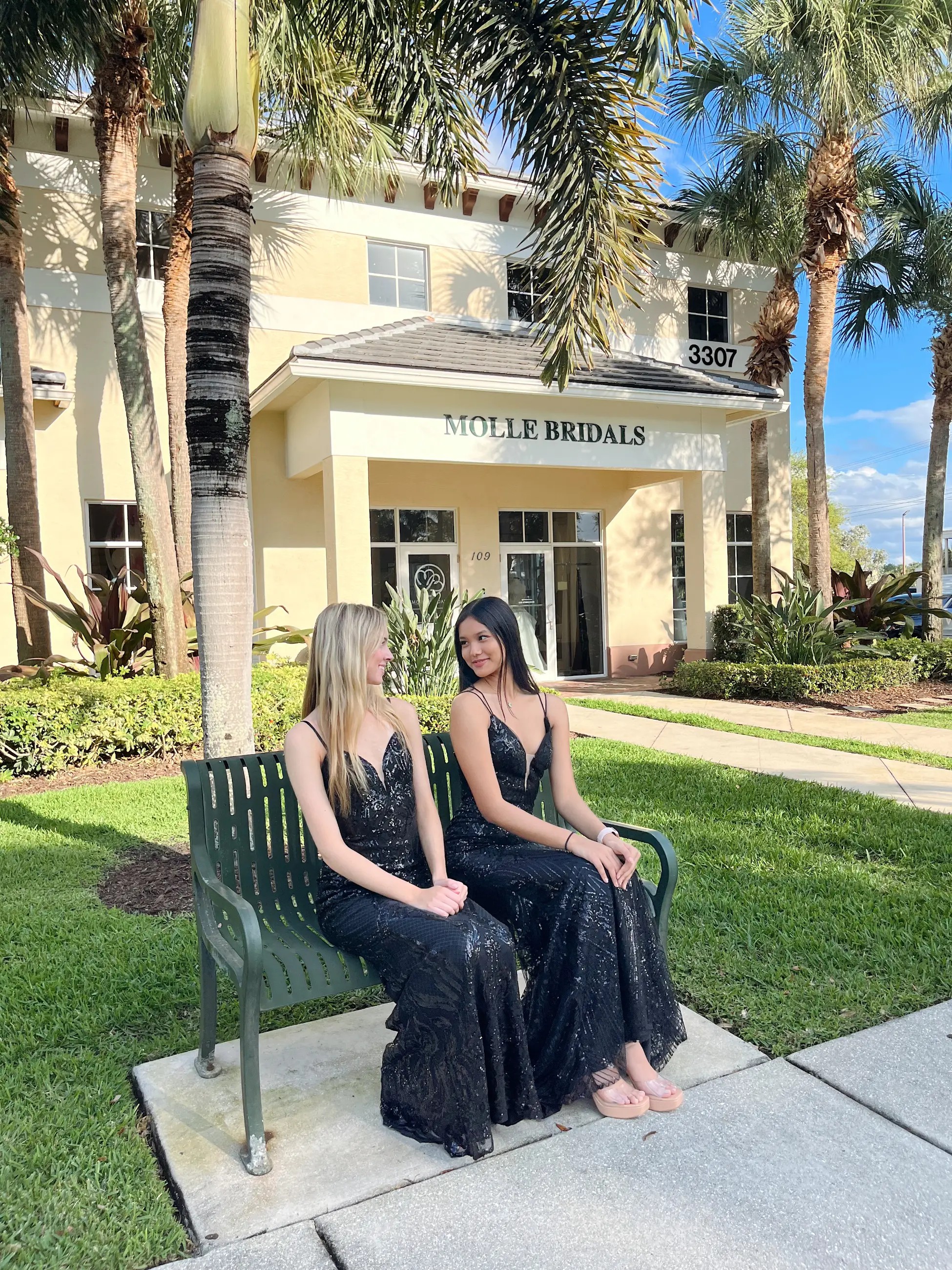 There are two models wearing black evening gowns with spaghetti straps and glittery fabric