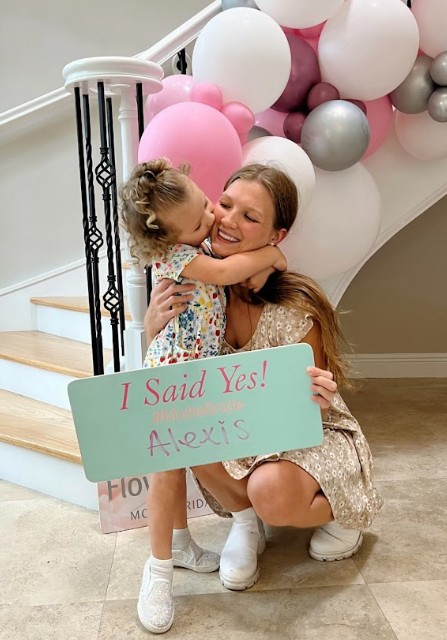 A woman kneels on the floor, holding a sign that says 