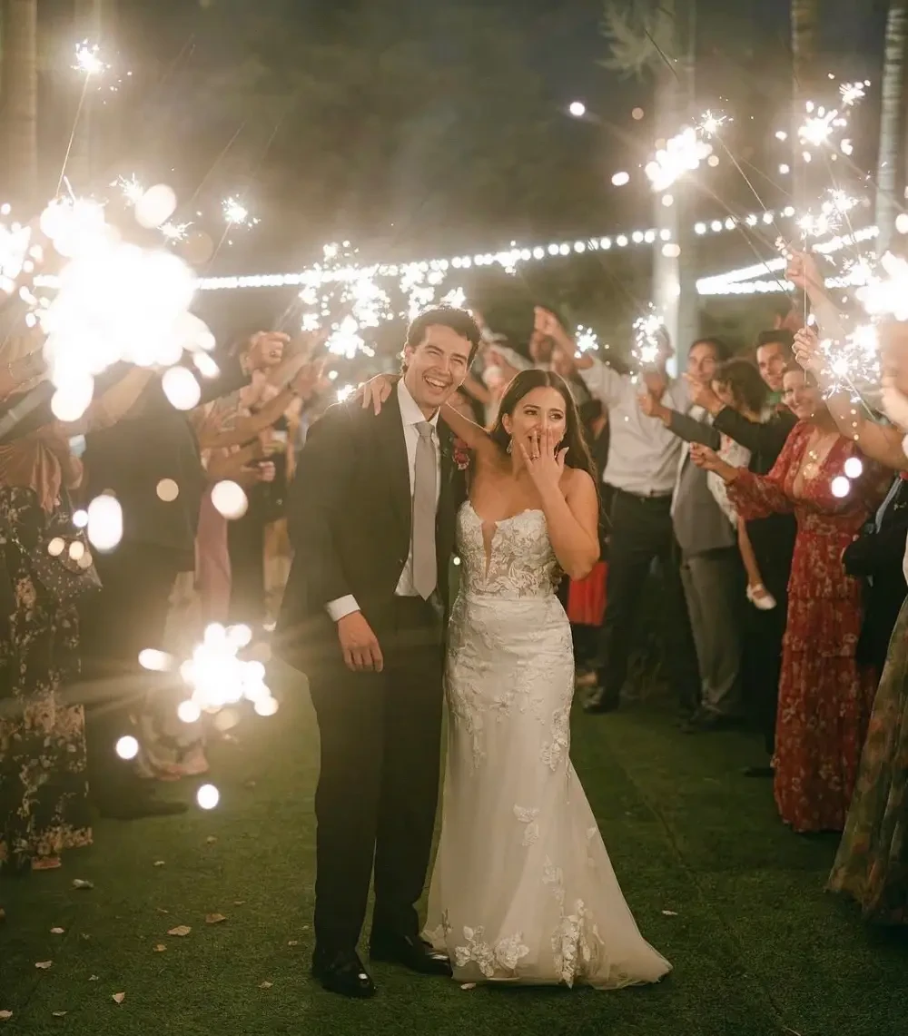A joyous wedding couple posing together while guests celebrate with sparklers around them.