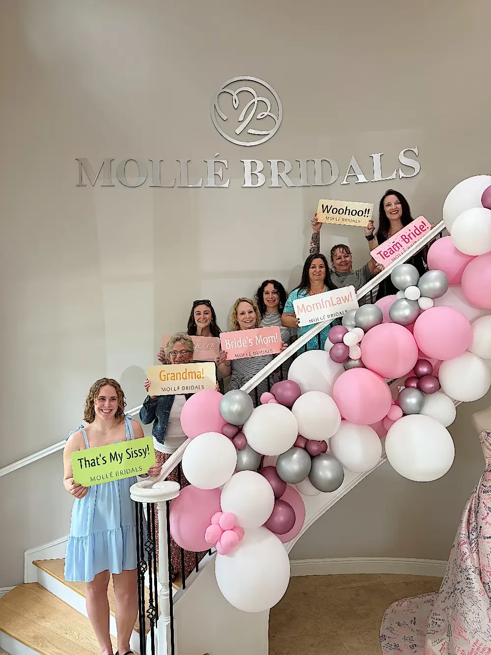 A group of women holding colorful signs standing on a staircase decorated with balloons, with a sign that reads 