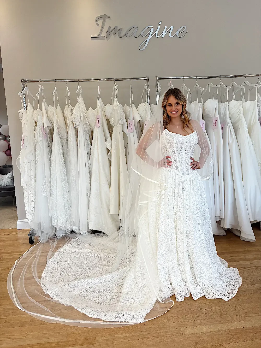 A bride poses in a wedding dress in front of a rack of white wedding dresses.