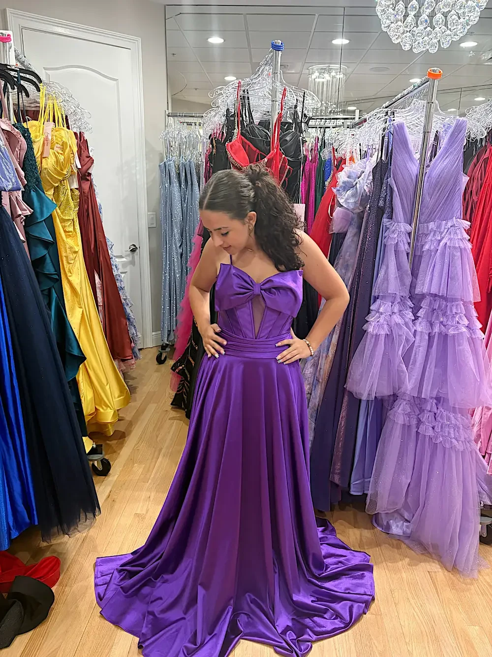 A person wearing a purple dress is standing in a clothing store surrounded by various dresses.