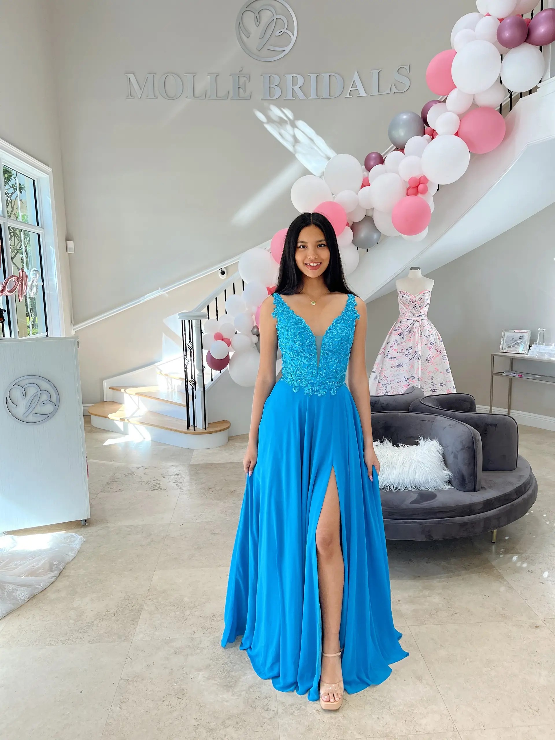 Model is wearing an a-line blue evening gown that is sleeveless and has a thigh high slit