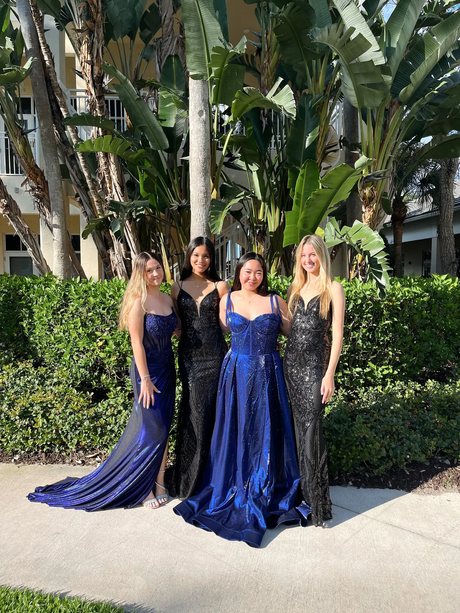 image shows four models wearing black and navy blue floor length evening gowns